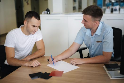 Man choosing and buying car at car showroom. Car salesman helps them to make right decision. Man sign documents.