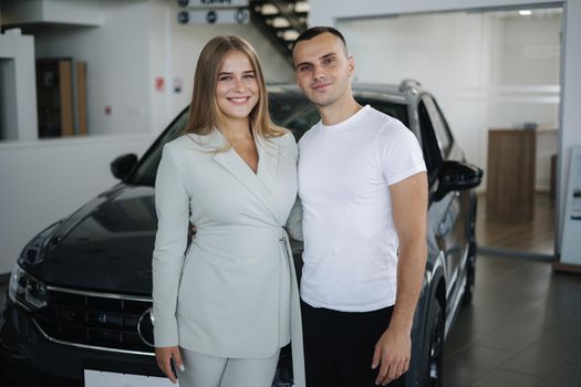 Portrait of beautiful young couple happy after buying new car from car showroom. Woman hus her man and glad.