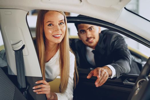 Man car dealer showing a woman buyer a new car in car salon