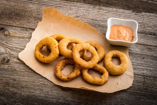 fried onion rings on parchment with sauce on a wooden background