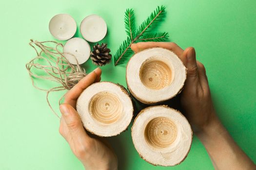 DIY Christmas candle holder made of pine logs, candles, craft rope, fir branches and cones. Hands fasten and tie the rope. Step-by-step instructions flat lay, step 3.