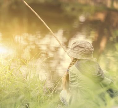 little fisher girl holds a rod sitting near a river