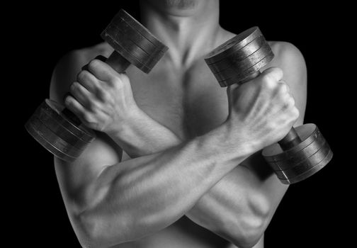 Muscular man holds dumbbells with arms crossed, monochrome image