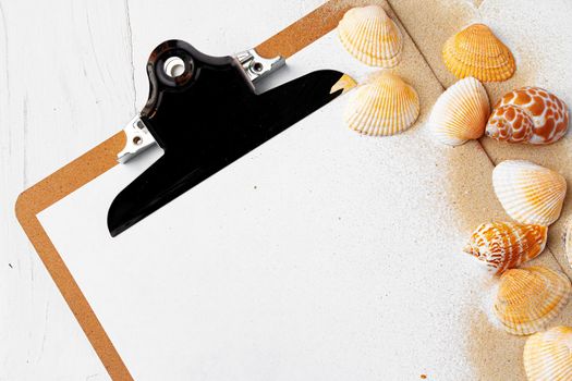 Clipboard with sea shells on white wooden table close up, copy space.