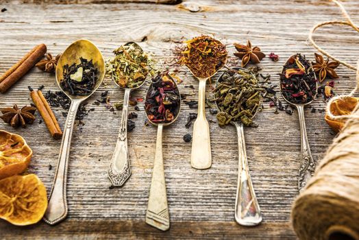 assortment of dry teas in silver spoons on wooden background