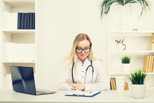 Young beautiful doctor woman working happy and smile in hospital, sitting on table, medical concept, toned