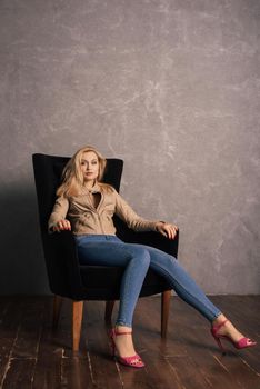 Adalt lady in jeans and a leather jacket sitting on the armchair having a rest