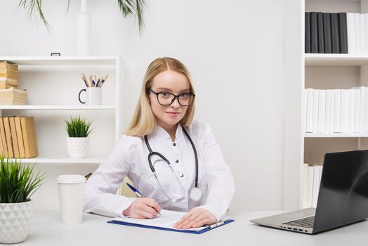 Young beautiful doctor woman working happy and smile in hospital, sitting on table, medical concept