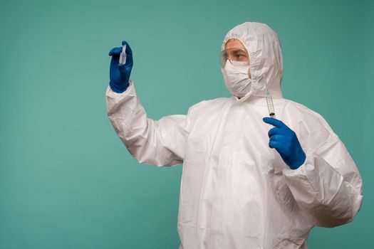 A male doctor in protective overalls and a mask holds an ampoule with a vaccine and syringe in his hands. Coronovirus protection concept in China. - image