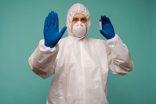 A male doctor in protective overalls and a mask holds an ampoule with a vaccine in his hands shows stop sign. Coronovirus protection concept in China. - image