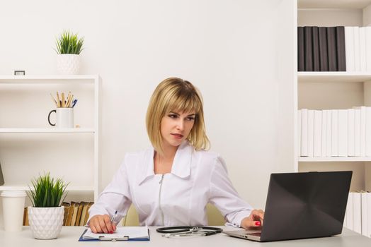 Friendly female doctor works at her desk in the office - image