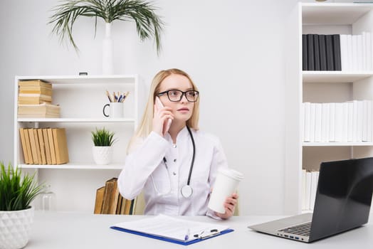 Portrait of a beautiful smiling woman doctor while talking on the smartphone and complete a medical information - Image