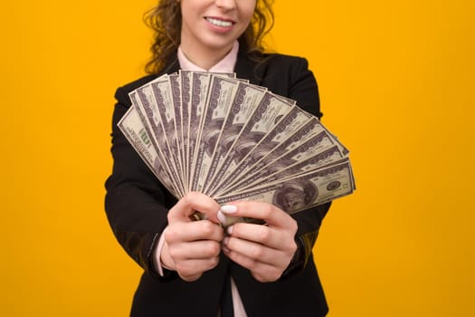 Woman showing a stack of money with her finger isolated on yellow background.