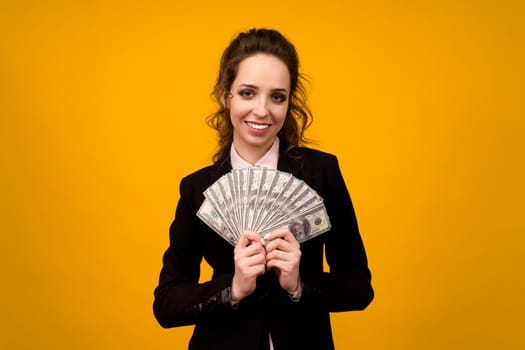 Woman showing a stack of money with her finger isolated on yellow background.