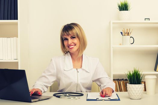 Friendly female doctor works at her desk in the office - image toned