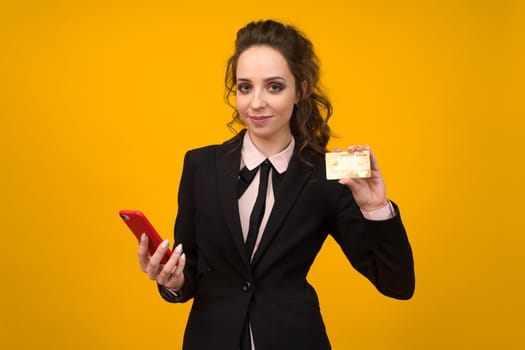 Photo of pleased young woman posing isolated over yellow wall background using mobile phone holding debit card. - image
