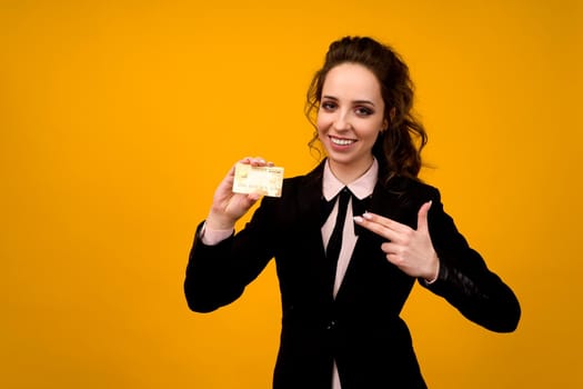 Portrait of a beautiful young business woman standing isolated over yellow background, holding credit card - image