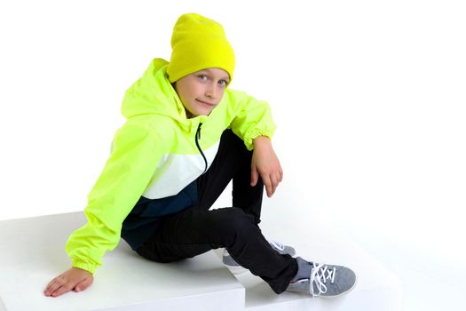 Cute stylish boy posing on staircase. Preteen boy wearing sports tracksuit with sweatshirt, pants and hat lying isolated on white background. Happy childhood, active healthy lifestyle concept