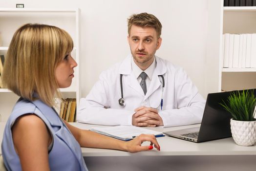 Young woman on a consultation with a male surgeon or therapist in his office. Selective focus on the doctor.