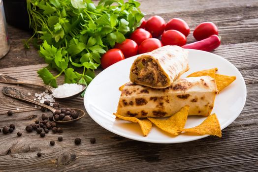 burrito with chips on plate and vegetables on a wooden background