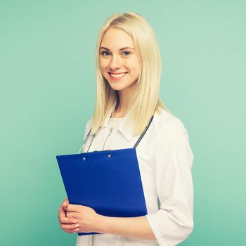 Portrait of an attractive young female doctor in white coat on blue background. toned