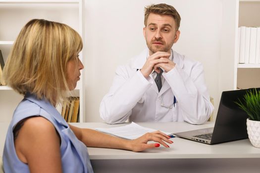 Young woman on a consultation with a male surgeon or therapist in his office. Selective focus on the doctor.