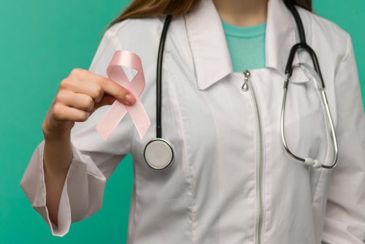Pink ribbon for breast cancer awareness in woman doctor's hand on blue background