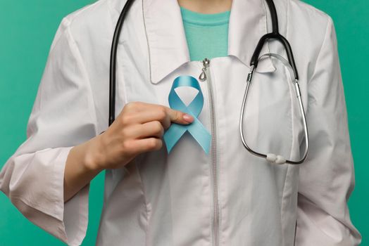 Blue ribbon for prostate cancer awareness campaign and men's health care concept with symbolic bow in doctor's hand - image