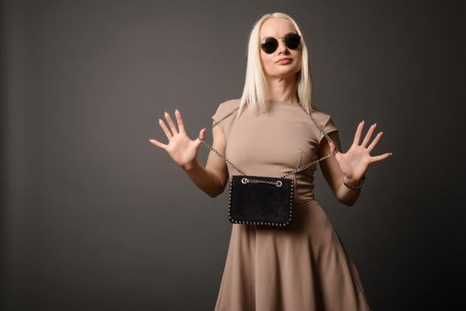 Beautiful girl with a handbag and sunglasses shows palms isolated on grey background