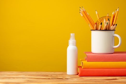 Back to school concept with stationery in cup and hand antiseptic spray against yellow background