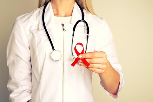 Female doctor withAID, HIV red ribbon. Cancer concept. Doctor Holds Red Ribbon to awareness world aids day Dec. 1. - Image