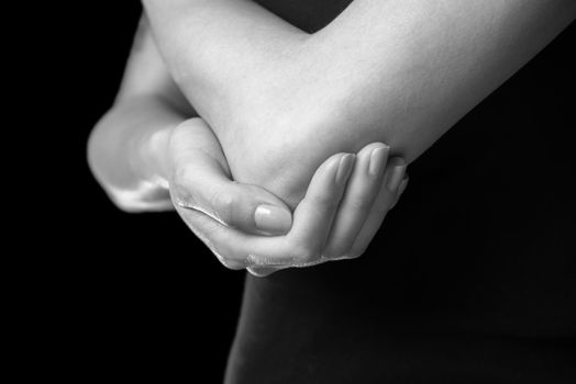 Unrecognizable woman holds her elbow joint, acute pain in the elbow, monochrome image