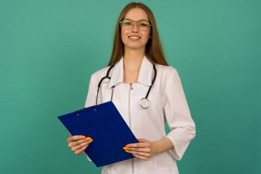 Beautiful young girl nurse or trainee doctor with blue folder and statoscope on a blue background - image