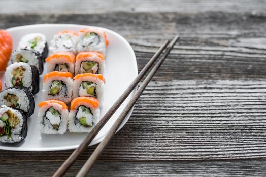 various sushi on white plate with chopsticks on wooden background