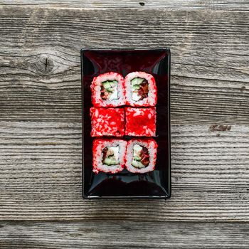 sushi on square black plate with chopsticks on wooden background