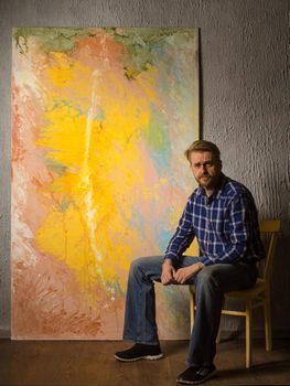 Portrait Of Male Artist sits next to his abstract painting in the Studio.