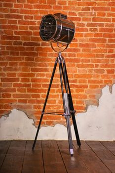 Old Fashioned Floor Lamp on Tripod near the brick wall.