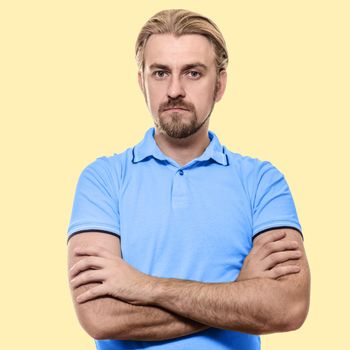 Stylish young man standing arms crossed in a blue T-shirt isolated on a yellow background