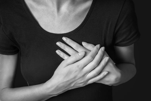 Woman is clutching her chest, acute pain possible heart attack, monochrome image