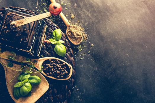 old mill and wooden spoons with spices on a black table
