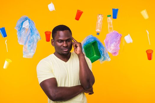Problem of trash, plastic recycling, pollution and environmental concept - pensive african american man on yellow background with garbage