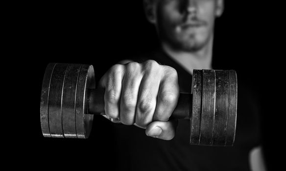 Muscular man holds dumbbell, focus on dumbbell, monochrome image