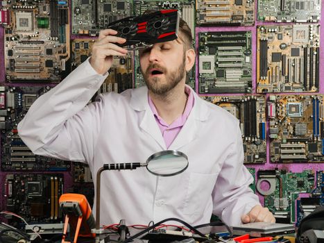 A young electronics engineer cools his forehead with a computer cooler while sitting at his lab table