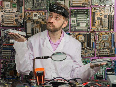 young male electrician engineer weighs in the hands of the hdd and drive sitting at the table of the electrical laboratory.