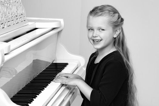 Beautiful little girl playing on white grand piano. Black and white shot of pretty long haired girl sitting at piano in living room. Cute child learning to play music instrument