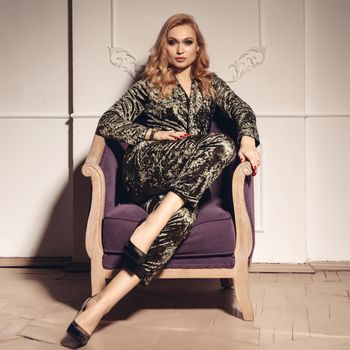 Portrait of a beautiful young woman sitting in a stylish evening gown on an ornate antique wooden armchair