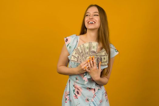 Joyful girl won the lottery and holds a fan of US dollars in her hands on a yellow background - image