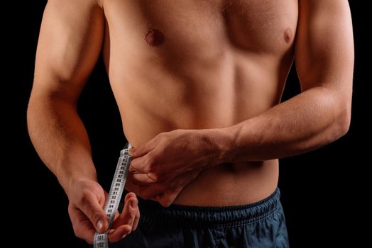 Sportsman is measuring waist with tape on a black background