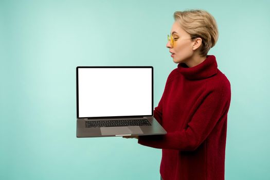 Young girl in a red sweater demonstrates a blank laptop screen on a blue background - image