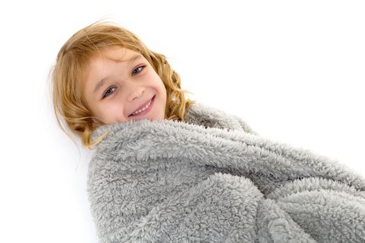 Cute happy girl lying on gray plaid. Pretty cheerful barefoot girl in stylish dress playing with soft blanket. Adorable blonde curly child isolated on white background